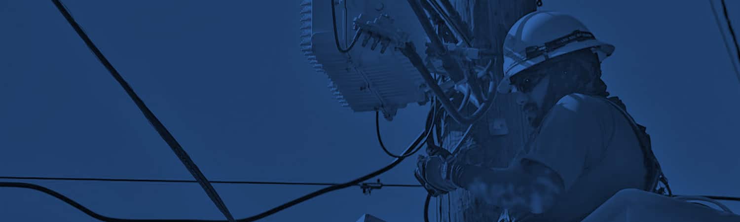 Photo of a man wearing a hard hat, working with wires on a telephone pole.